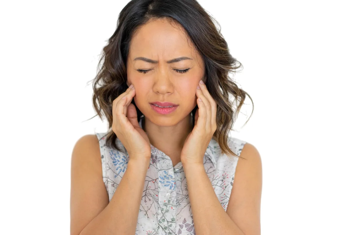 Woman pressing her fingers to both sides of her jaw in discomfort from TMJ pain